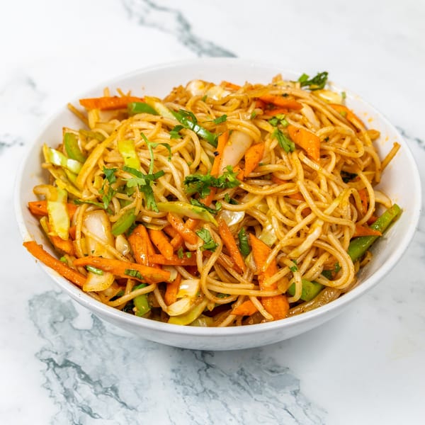 A white bowl filled with Mirch Masala's Indian noodles, carrots, green peppers, and cilantro.