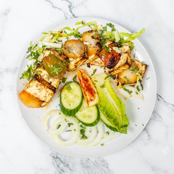 Grilled paneer, bell peppers, and onions with a side salad of lettuce, cucumbers, and onion rings.