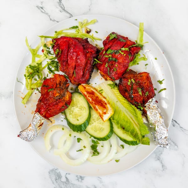 Four Mirch Masala Indian Restaurant chicken drumsticks, garnished with cilantro, cucumber, onions, and lettuce.
